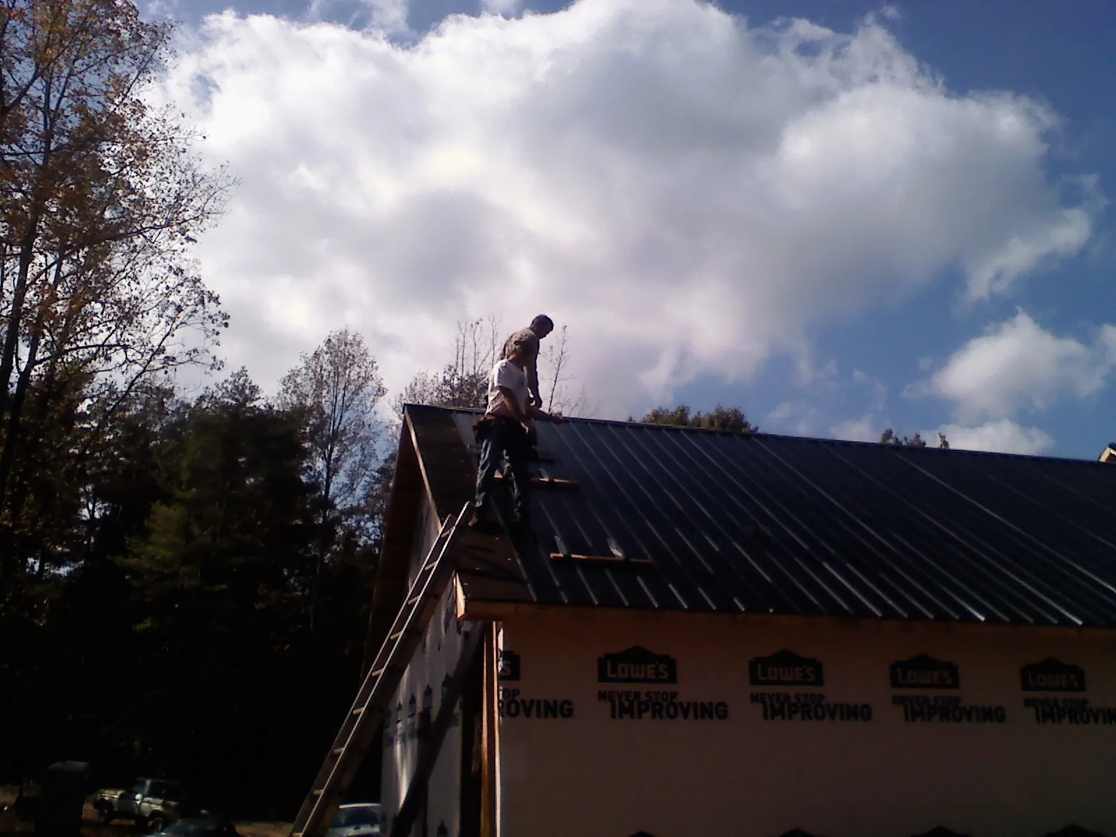Roofer fastening dark metal panels high against a cloudy sky, from a Roof Inspection job in Durham