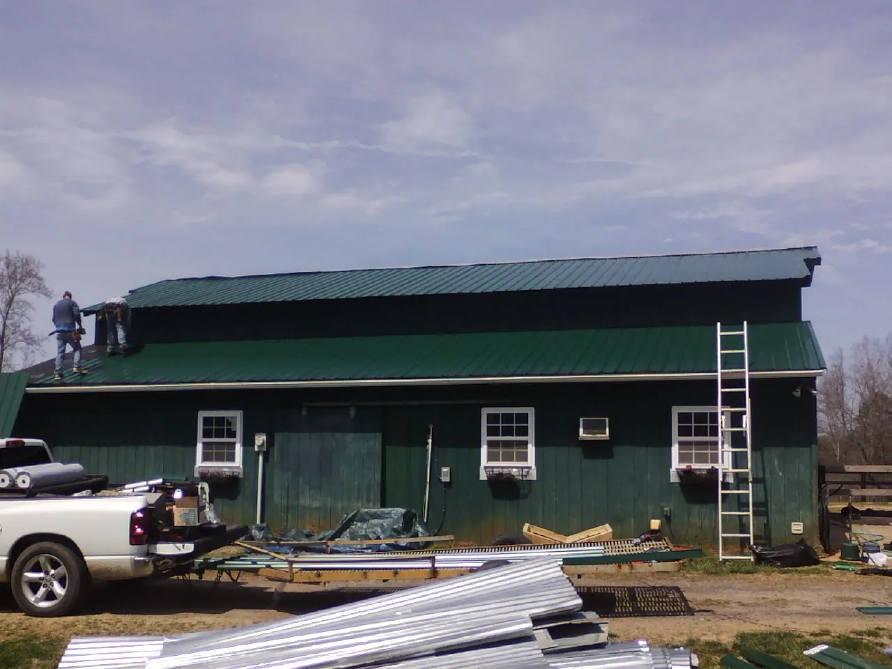 Crew installing green metal roofing on a large green barn in Durham